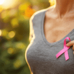 Frau in grauem Oberteil hält rosa Brustkrebs-Bewusstseins-Schleife im Freien mit weichem Bokeh-Hintergrund