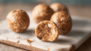 Kalorienarme Energy Balls ohne Datteln mit Haferflocken und Erdnussbutter auf rustikalem Holzbrett, einer halbiert