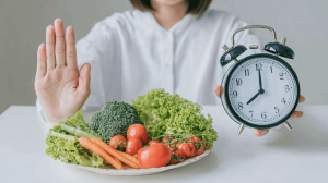 Heilfasten: Frau mit Wecker und gesundem Gemüse zeigt Fastenzeit und pflanzliche Ernährung