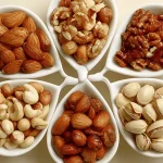 Verschiedene Nusssorten in weißen Schalen zur natürlichen Cholesterinsenkung: Walnüsse, Mandeln, Cashews, Haselnüsse für gesunde Herzfunktion