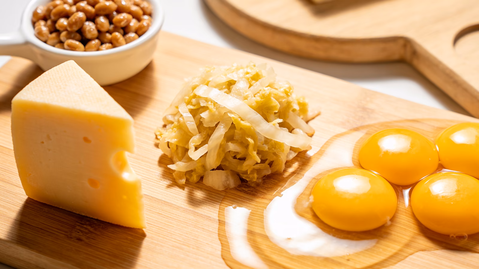 Vitamin-K2-reiche Lebensmittel wie Natto, gereifter Käse, Sauerkraut und Eigelb auf hellem Holztisch