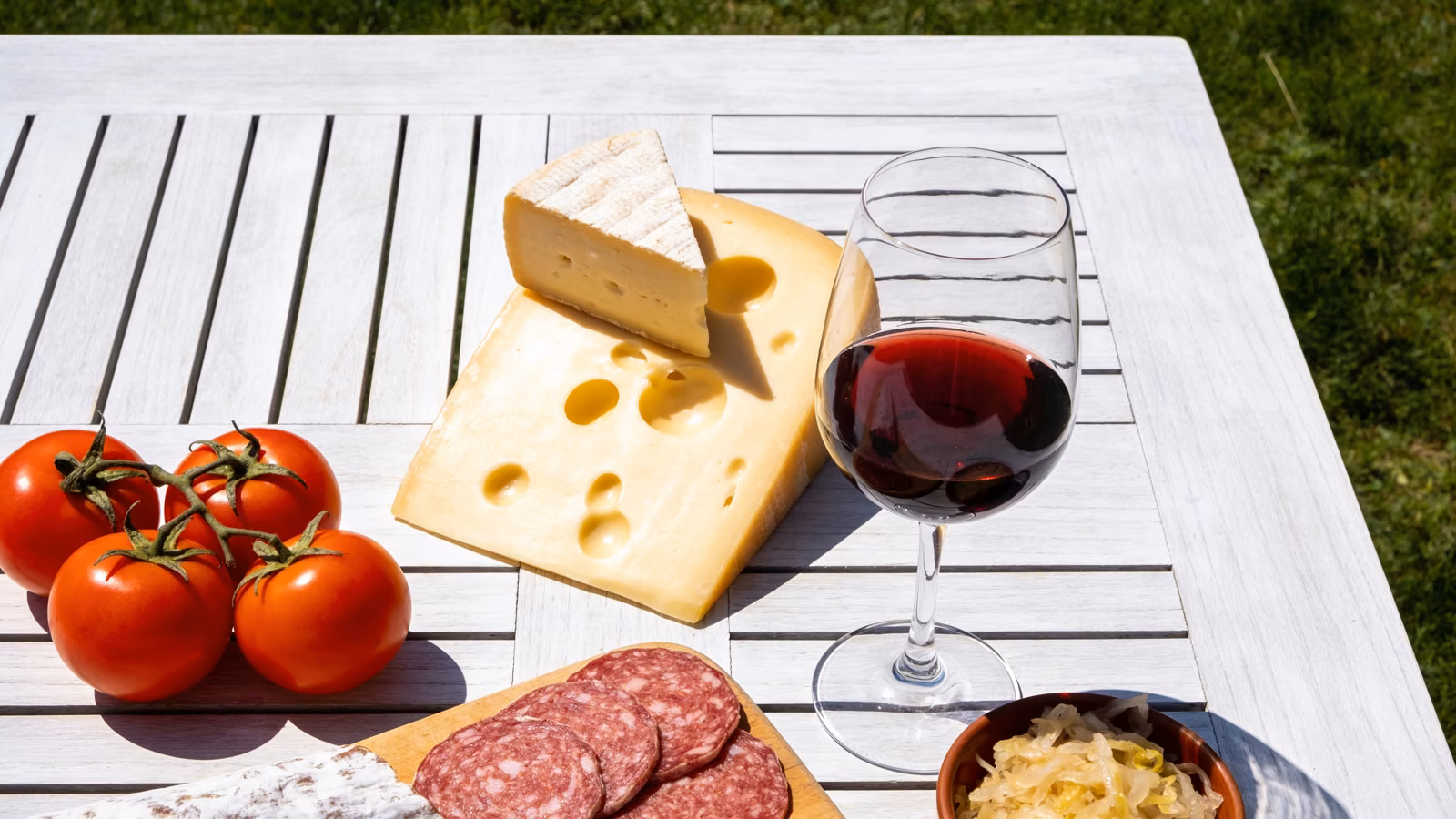 Histaminreiche Lebensmittel wie gereifter Käse, Rotwein, Tomaten und Salami auf hellem Holztisch