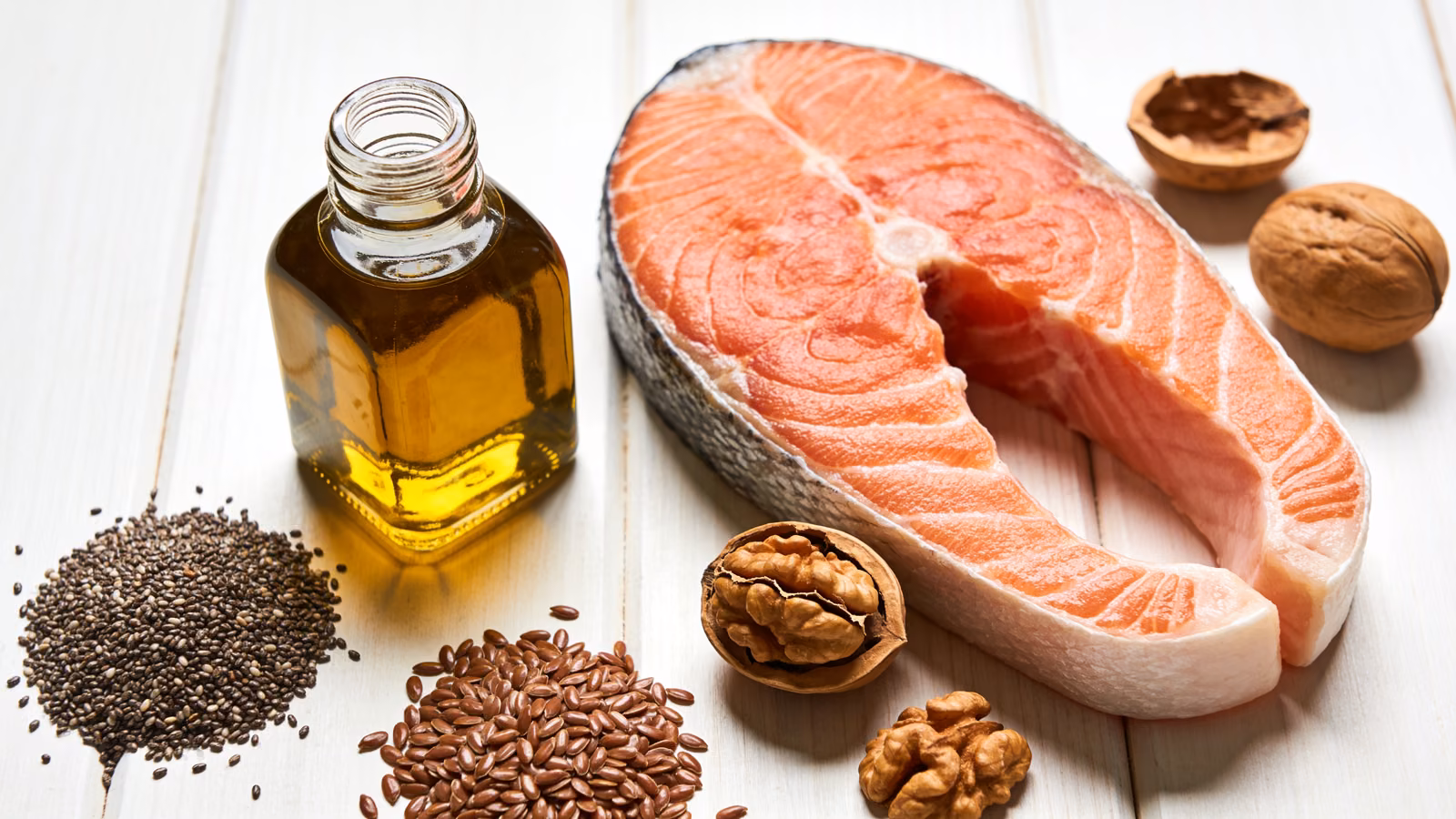 Omega-3-reiche Lebensmittel wie Lachs, Walnüsse, Chia- und Leinsamen und Öl auf hellem Holztisch