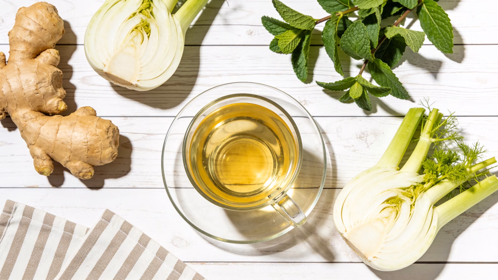 Verdauungsfreundliche Lebensmittel wie Ingwer, Fenchel, Pfefferminze und Kräutertee auf hellem Holztisch