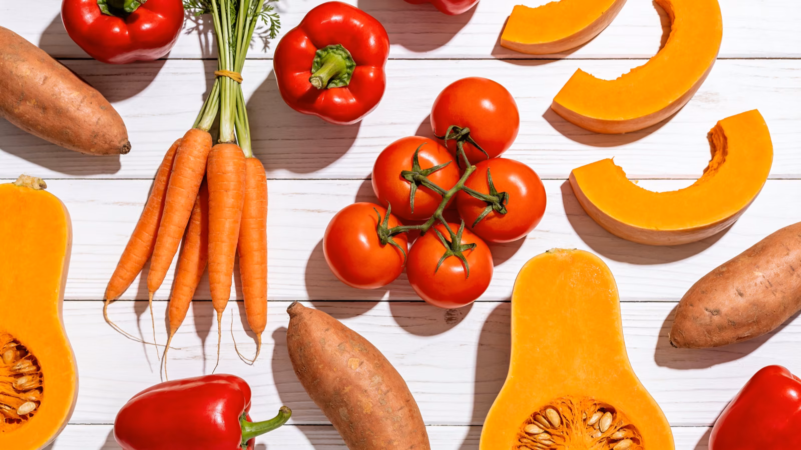 Carotinoidreiches Gemüse wie Karotten, Paprika, Tomaten und Kürbis auf hellem Holztisch