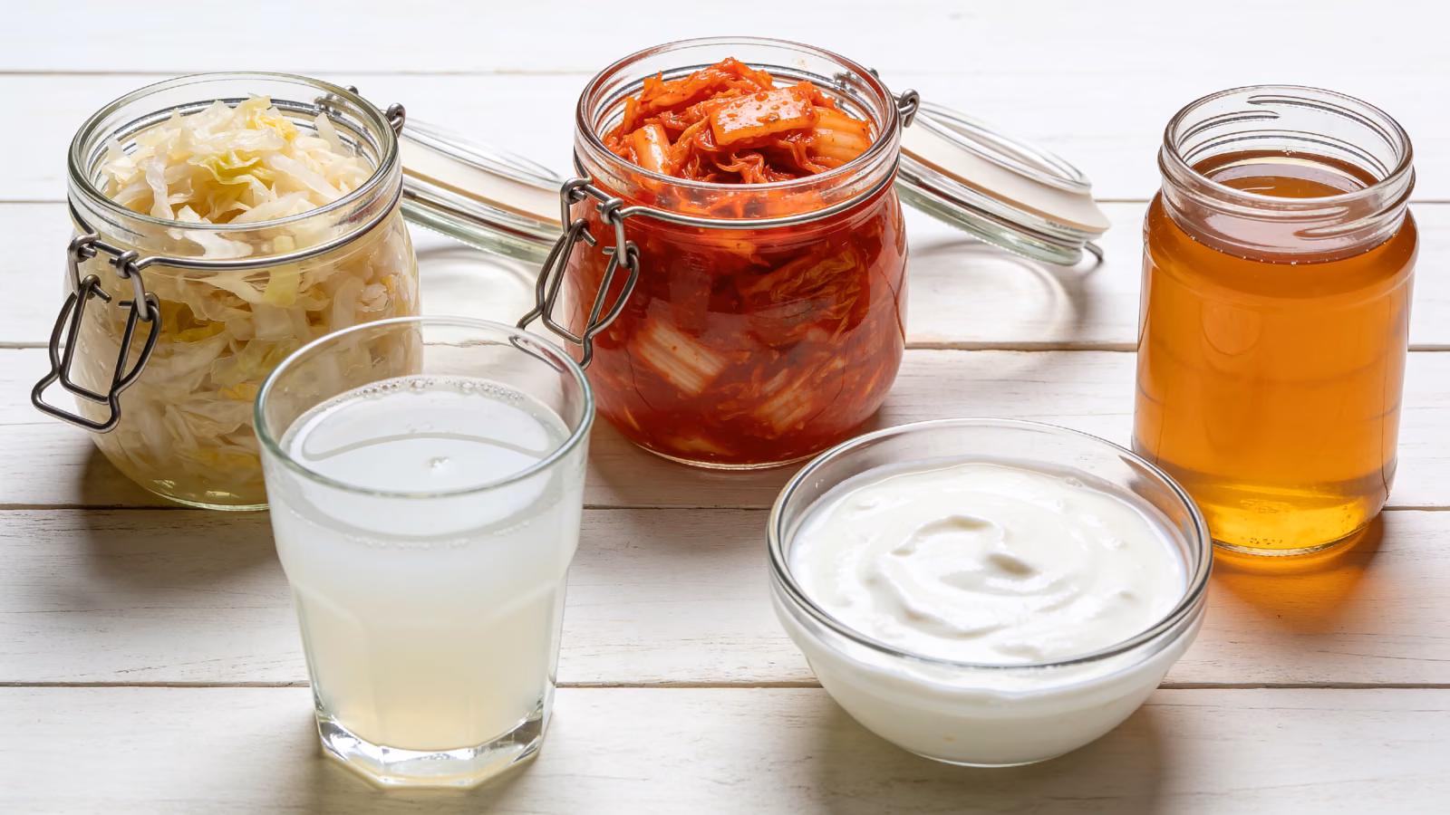 Fermentierte Lebensmittel wie Sauerkraut, Kimchi, Kefir und Joghurt in Gläsern auf hellem Holztisch