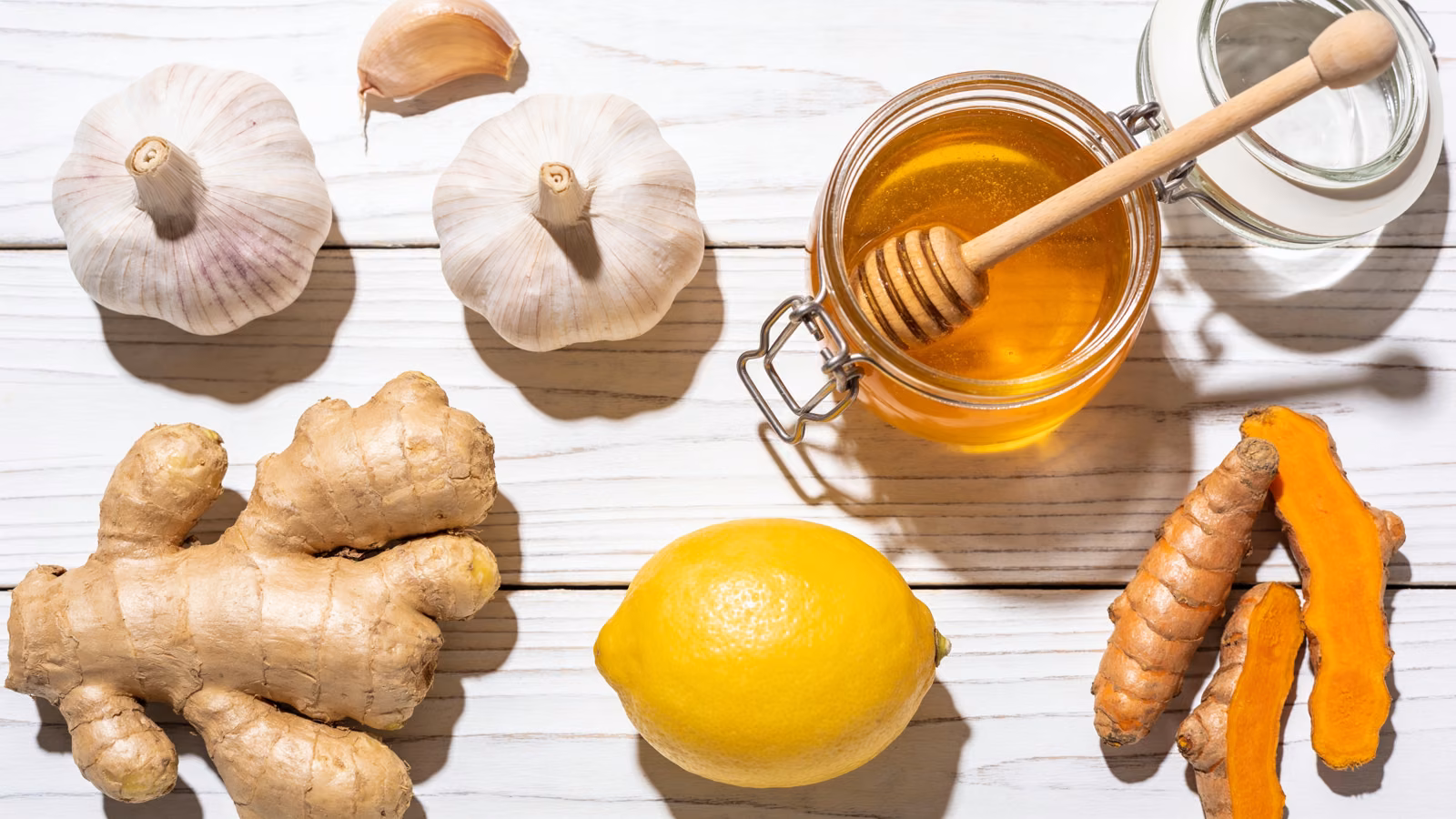Natürliche Hausmittel wie Knoblauch, Ingwer, Honig, Zitrone und Kurkuma auf hellem Holztisch
