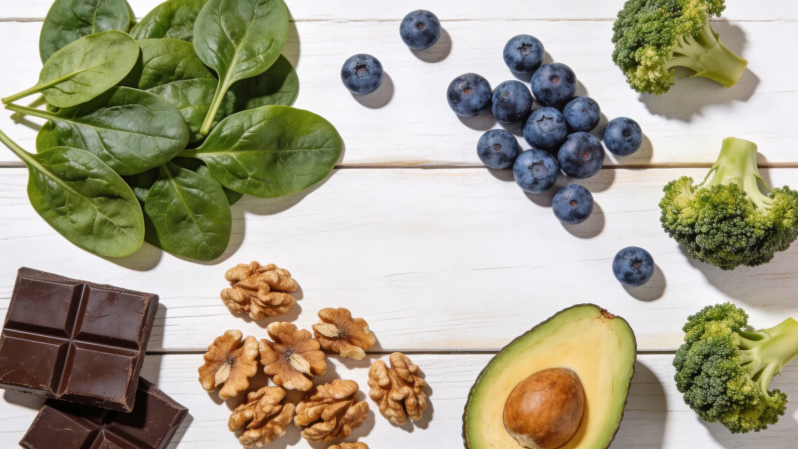 Antioxidantienreiche Lebensmittel wie Spinat, Blaubeeren, Walnüsse, Avocado und Brokkoli auf hellem Holztisch