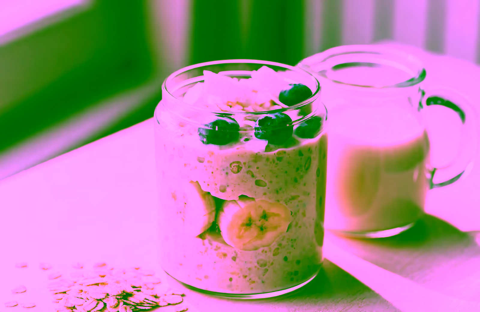 Overnight Oats mit Pflanzendrink, Banane und Blaubeeren neben einem Krug Mandelmilch
